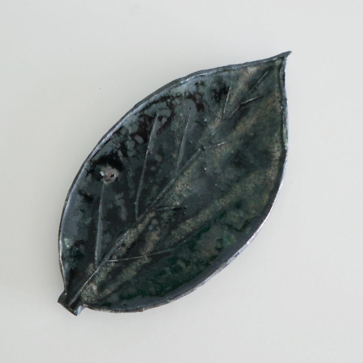 Leaf-shaped dish in dark green and black glaze with the leaf veins pressed into its surface.