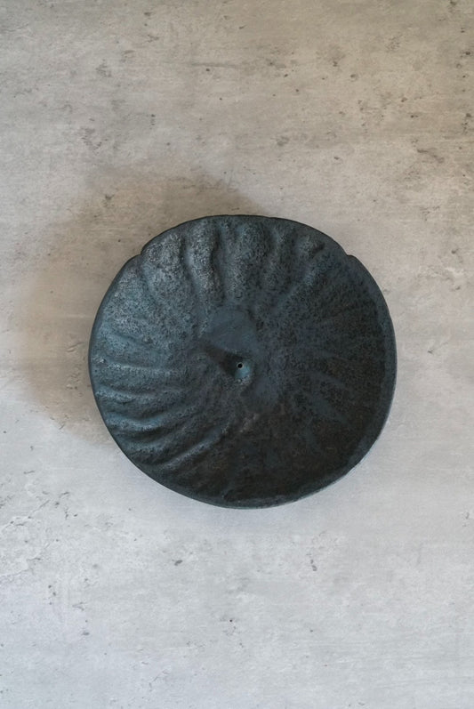 Round incense stand in dark blue-grey, its surface ribbed in a soft spiral from the centre.