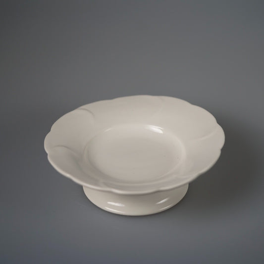 White footed plate with a softly lobed petal rim, lit against pale grey.