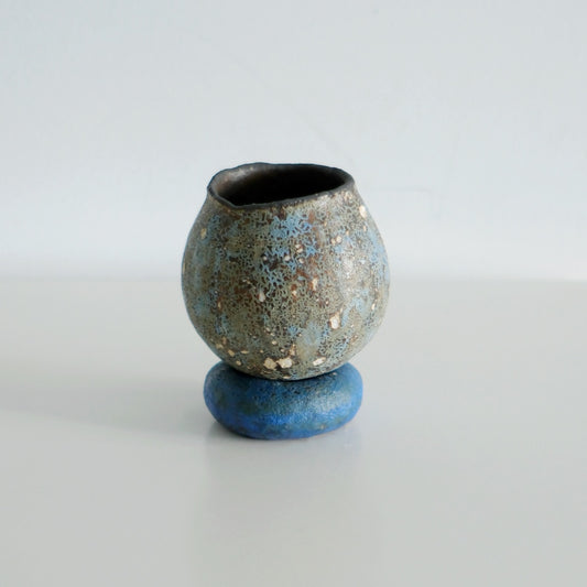 Small speckled blue-grey cup standing on a matching round blue saucer, on white.