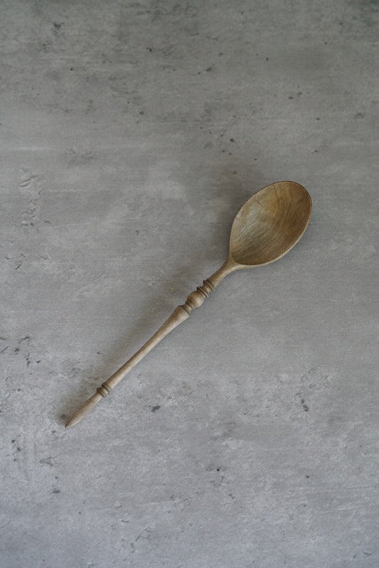 Carved wooden spoon with a pale oval bowl and a slim dark twisted handle, on grey concrete.