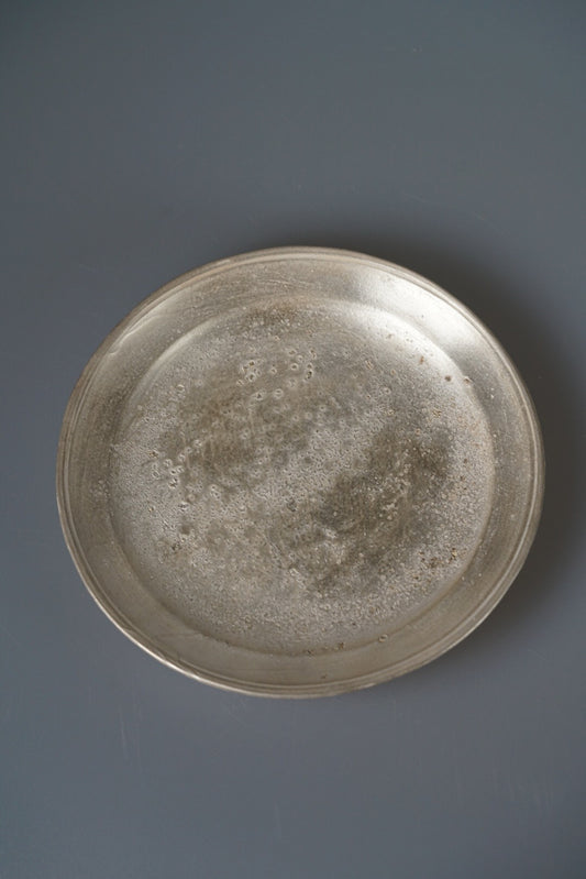 Round plate in mottled silver lustre with a raised rim, seen from above on grey.
