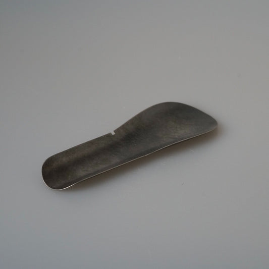 Broad stainless steel tea scoop with a curved shovel head and a short flat handle.