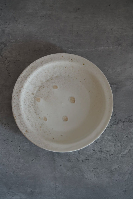Round white porcelain plate seen from above, its face marked with a few dark firing spots.