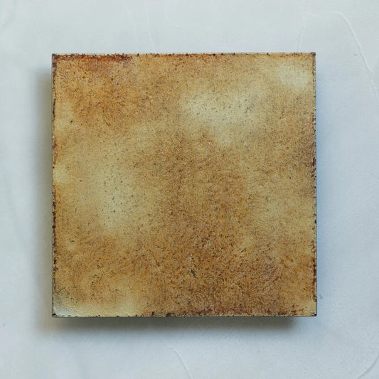 Square serving dish in mottled tan and rust, its surface like weathered paper, on a pale blue ground.
