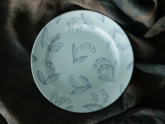 Pale porcelain plate drawn in fine grey line-work with sprigs of lily of the valley.