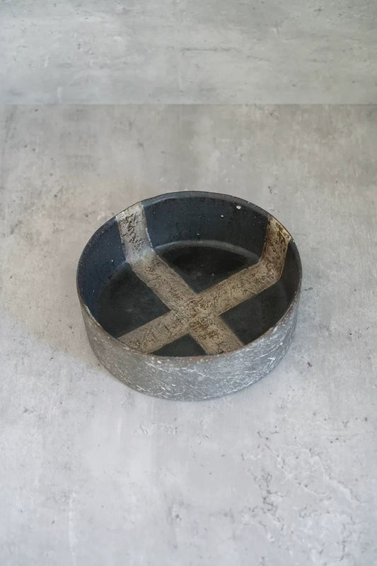 Round dark tray with a raised rim, marked with a broad pale cross across its well.