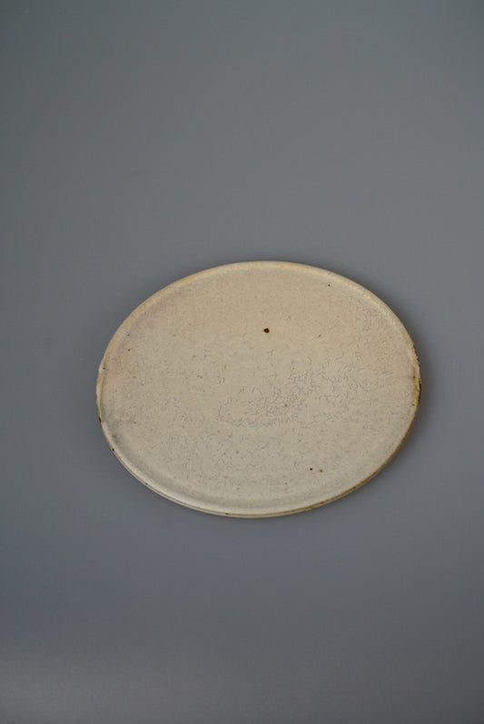 Plain round plate in speckled sandy cream with a barely raised rim, on grey.