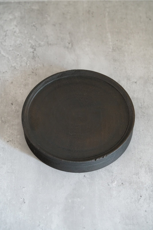 Round wooden tea tray with a raised rim, finished in dark matte lacquer over visible grain.