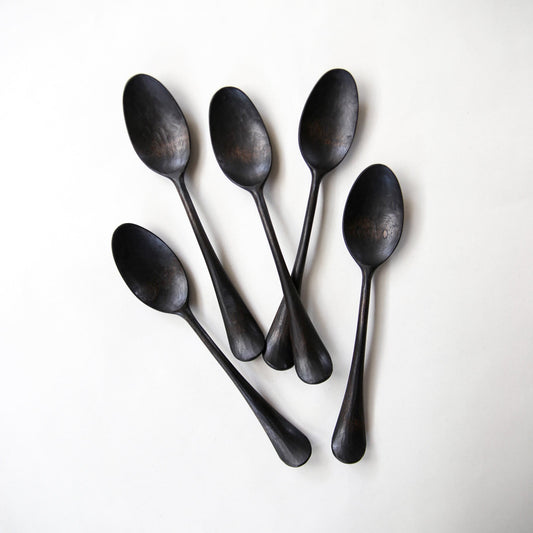 Five long black lacquer spoons with narrow handles, fanned out on a pale ground.