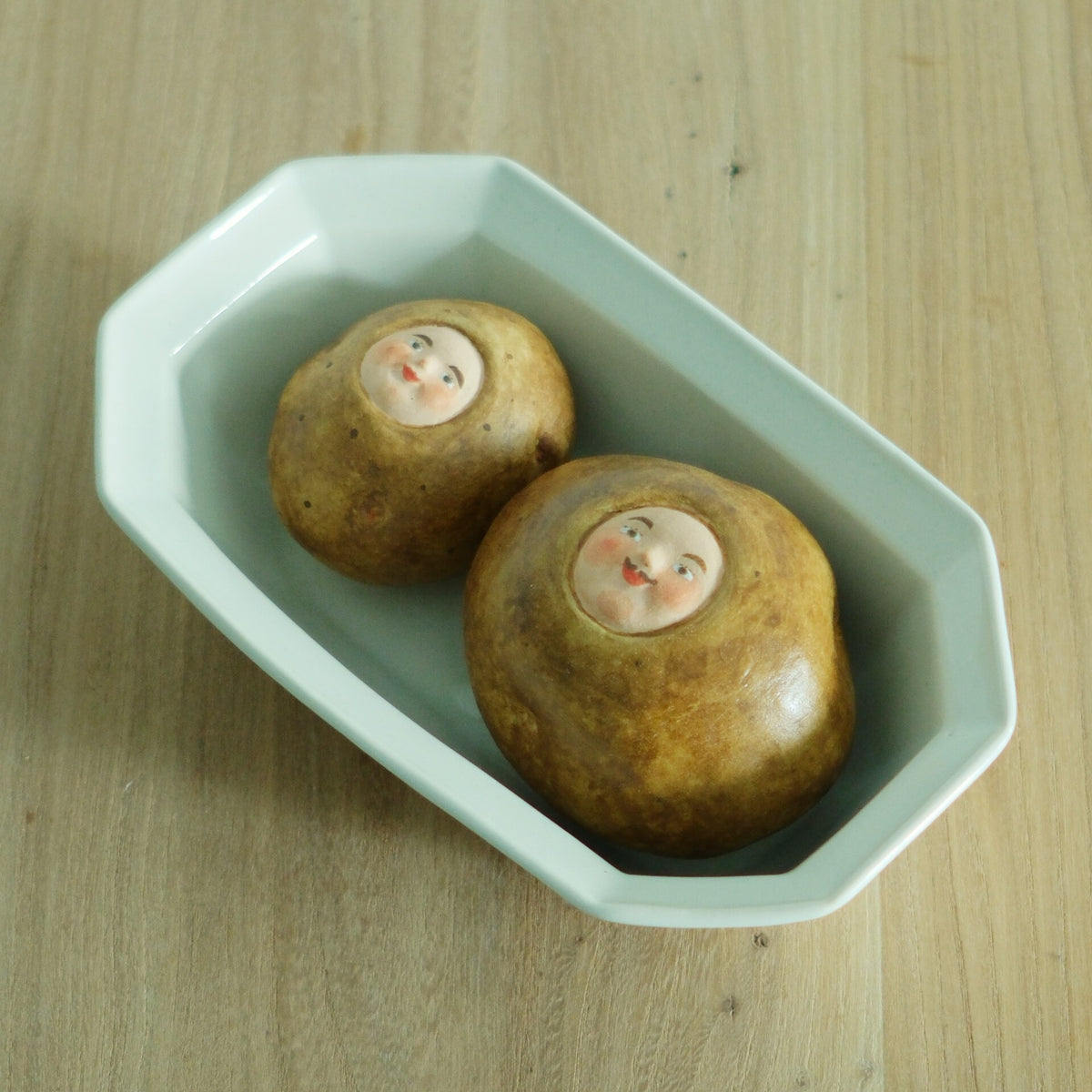 Octagonal bowl in pale mint green holding two small ceramic sweets with painted faces.