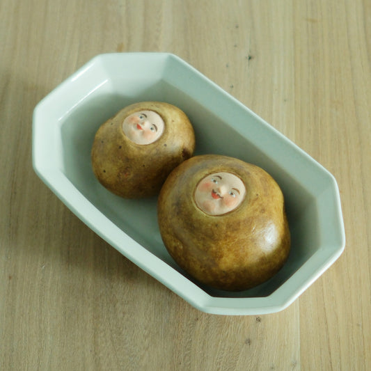 Octagonal bowl in pale mint green holding two small ceramic sweets with painted faces.