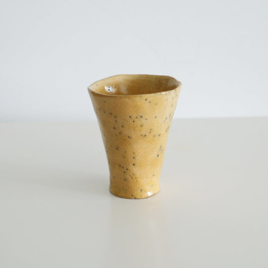 Flared cup in speckled ochre yellow with a softly uneven rim, lit against white.