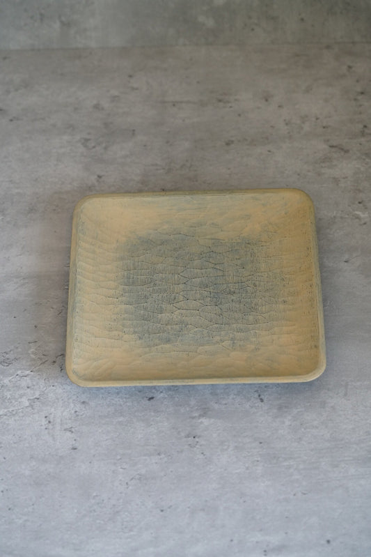 Square wooden plate finished in pale cream lacquer with a soft green shadow at its centre.