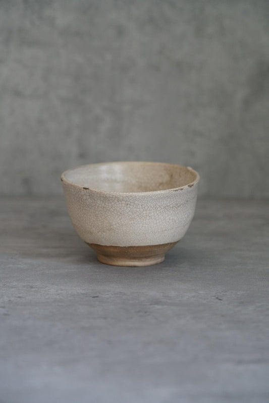 Small footed bowl in chalky cream slip with a bare brown clay foot, on grey concrete.