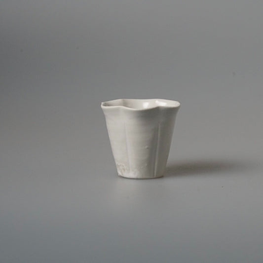 Small white tea cup with fluted sides and a gently folded rim, on pale grey.