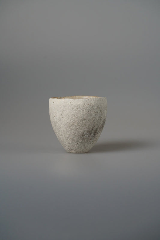 Small cream cup with a coarse sandy surface and a softly flaring rim, on pale grey.