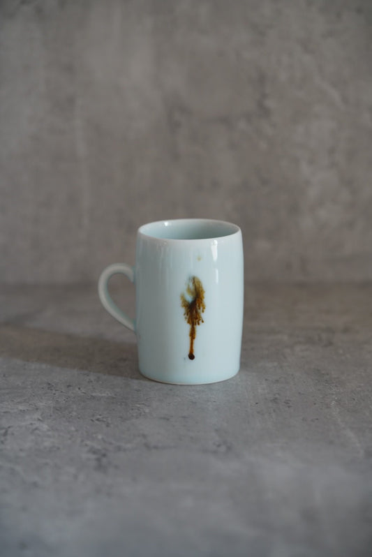 Tall white porcelain mug painted with a small gold figure, with a slim ring handle.