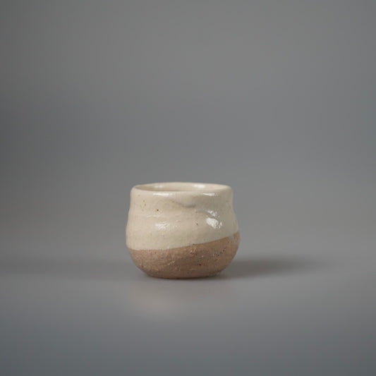 Small cream cup with a bare sandy clay base and a softly uneven rim.