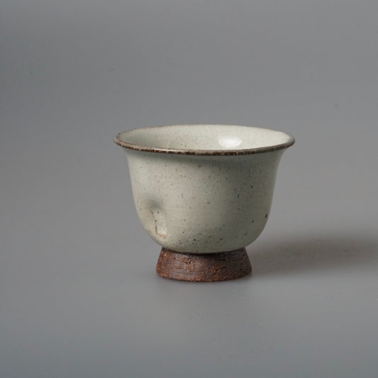 Flared cream cup on a rust-brown foot, its glaze finely speckled with dark flecks.