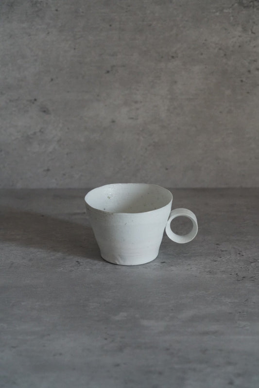 Small white porcelain mug with a thin ring handle, on a pale grey ground.
