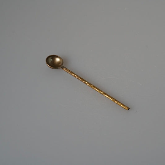 Slim brass coffee spoon with a small round bowl and a finely textured handle.