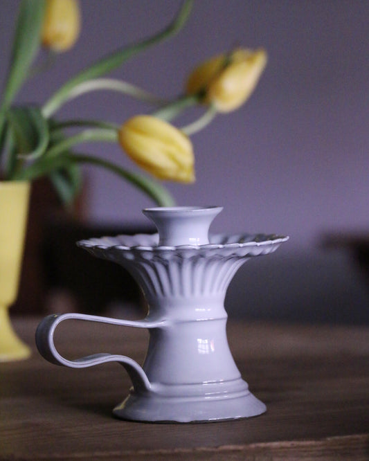 Pale lilac fluted candle holder with a wide frilled top and a loop handle, yellow tulips behind it.