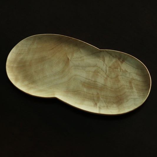 Wooden plate cut in a soft peanut shape, its pale golden grain glowing against black.