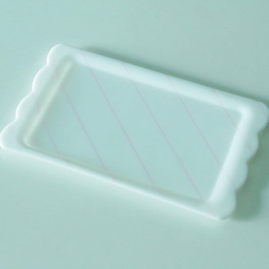 Rectangular pale blue-white glass plate with fine diagonal lines and a scalloped edge at one end.
