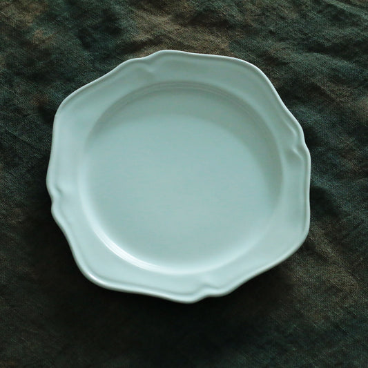Round celadon plate in soft blue-green with a gently scalloped edge, on dark cloth.
