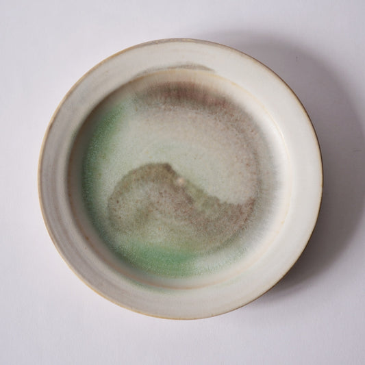 Wide cream plate with a raised rim and a ring of soft green and brown glaze around its well.