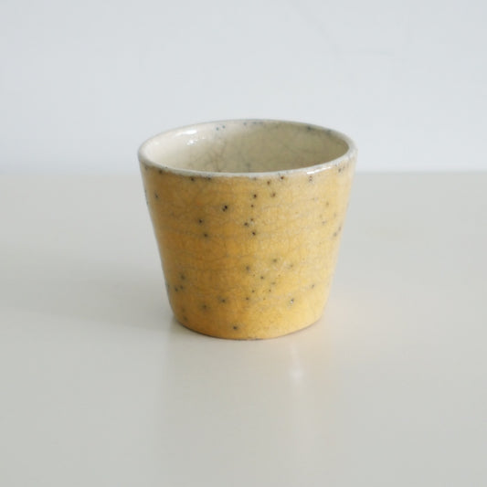 Tapered cup in warm speckled yellow with a smooth pale rim, lit against white.