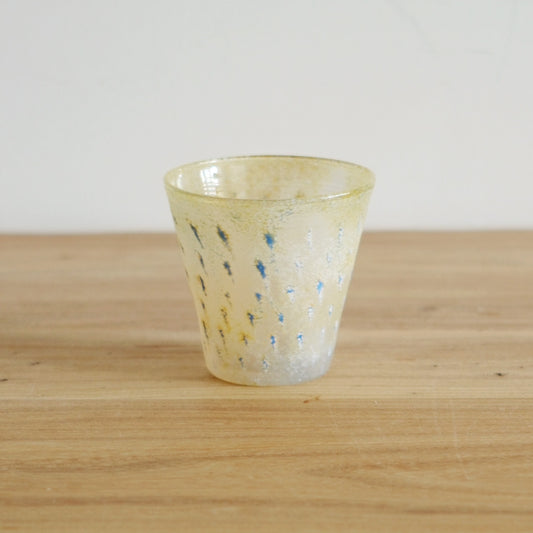 Pale yellow glass cup speckled with small blue flecks and a frosted, sugary surface.