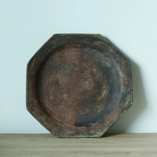 Octagonal plate in mottled rust brown and slate blue, standing upright on a wooden shelf.