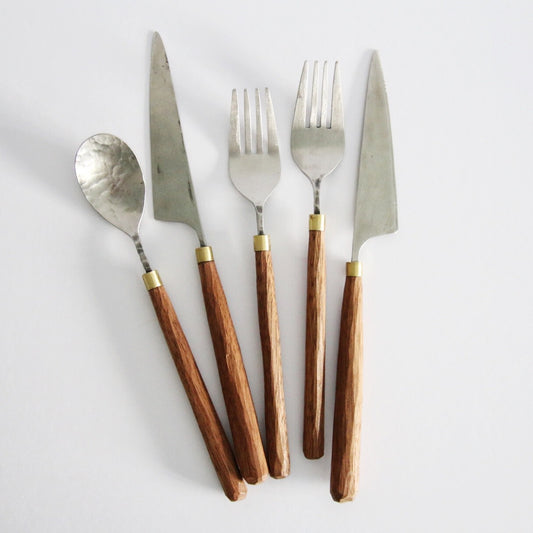 Five pieces of cutlery with turned wooden handles and brass collars, laid in a fan on white.