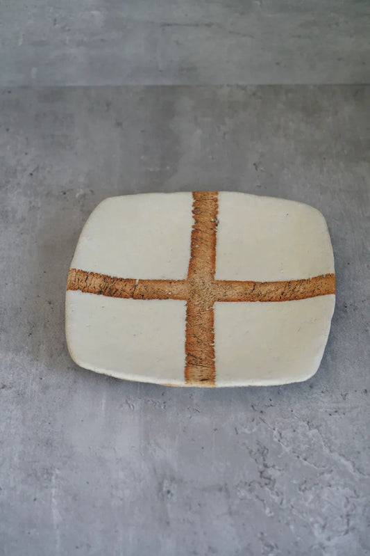 Square cream tray with rounded corners, marked with a broad rust-orange cross.