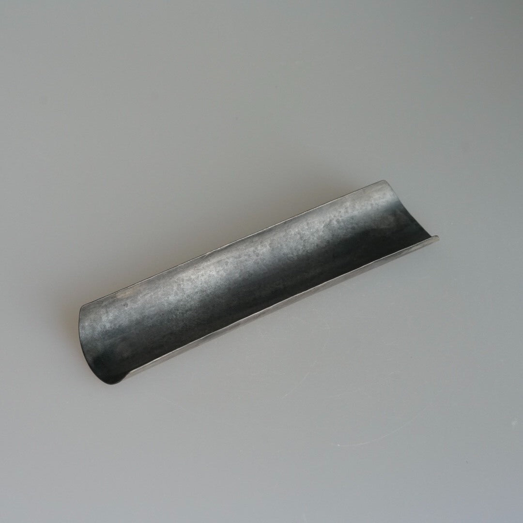 Long narrow metal tea scoop with a rolled channel, finished in mottled pewter grey.