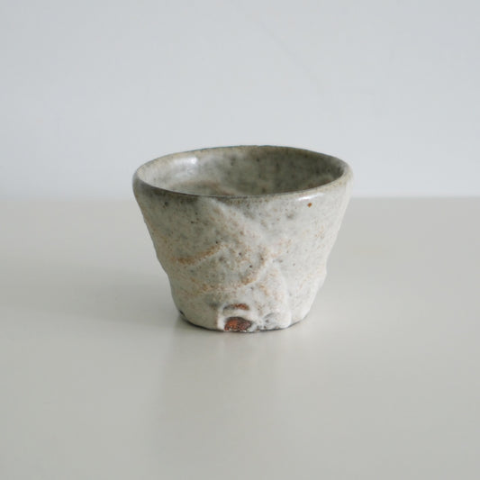 Tapered cup in chalky pale grey with a coarse, pitted surface and small rust flecks.