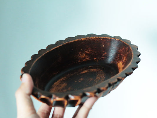 Oval bowl with a scalloped rim held in a hand, its interior glazed deep glossy brown.