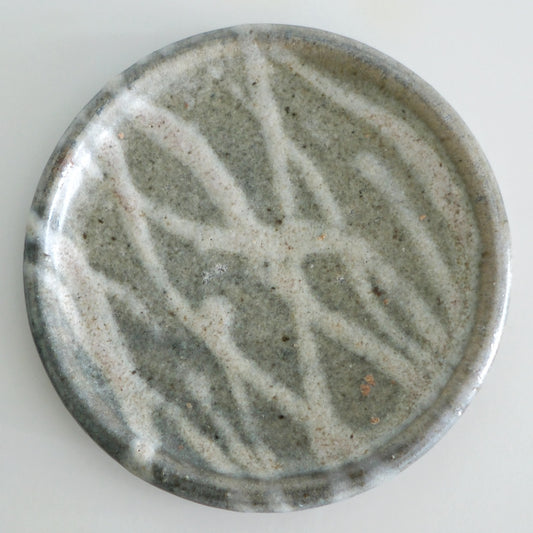 Round grey plate swept with broad strokes of cream slip across its speckled face.