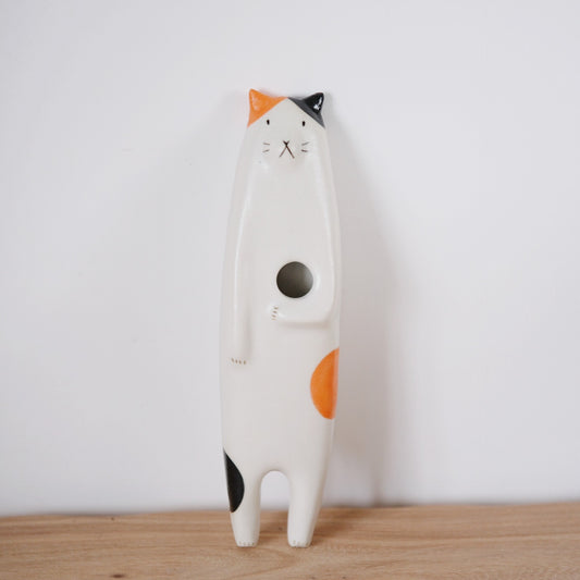 Tall standing ceramic cat in white with orange and black patches and a round opening in its belly.