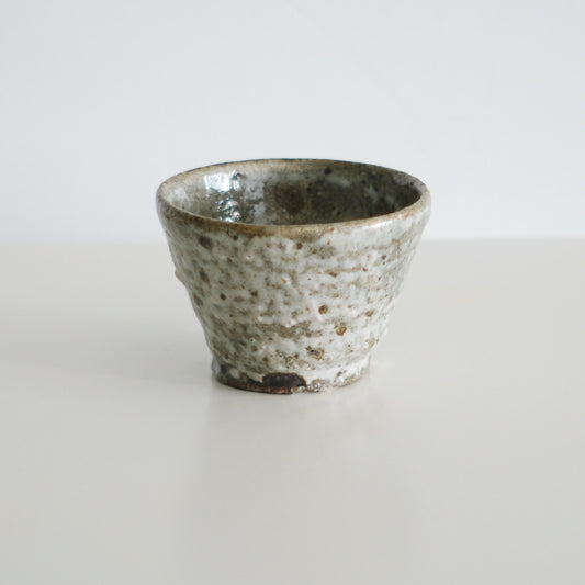 Small rough-textured cup in mottled cream and brown with a thin glazed rim.