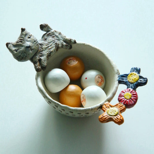 Cream bowl of round eggs with a grey cat modelled climbing over one rim and a flower on the other.