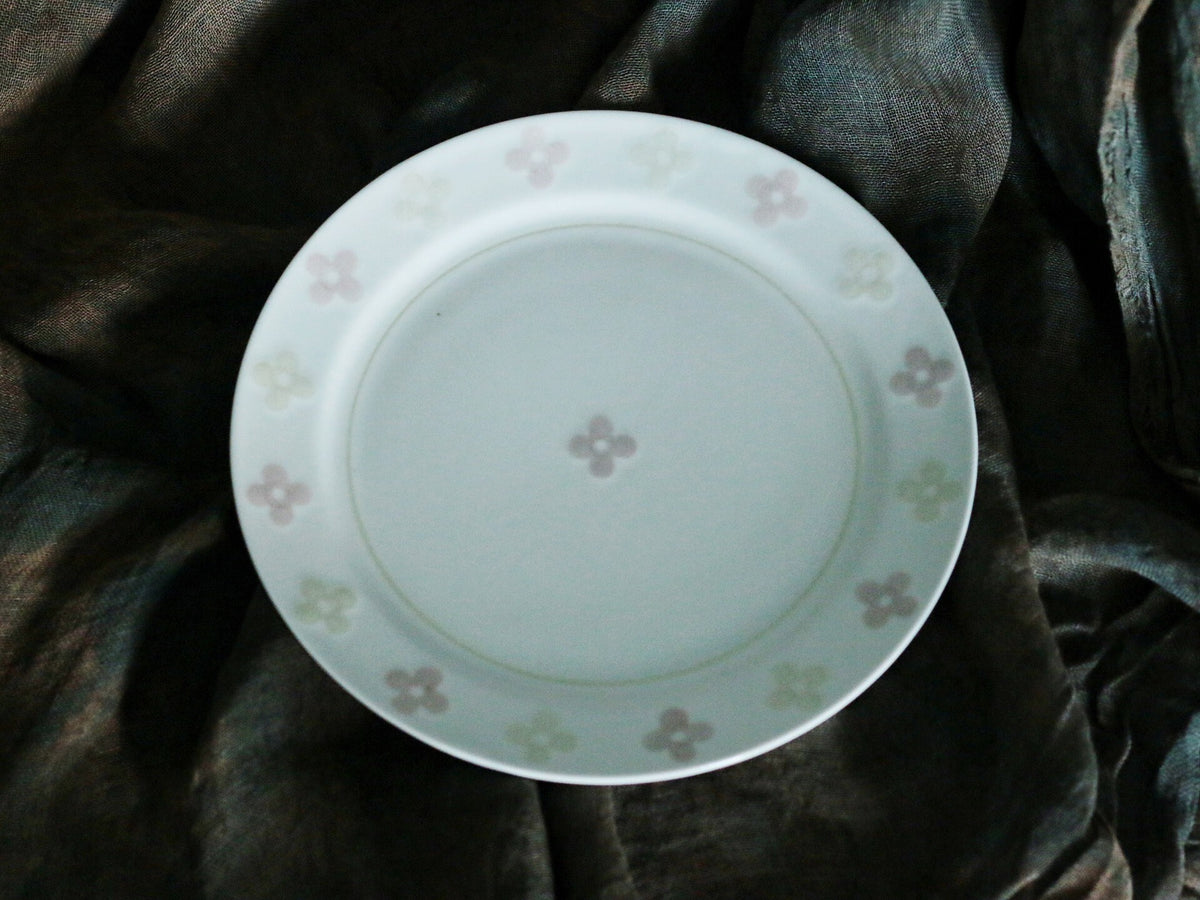 White porcelain plate scattered with small pale pink four-leaf clover motifs, on dark cloth.