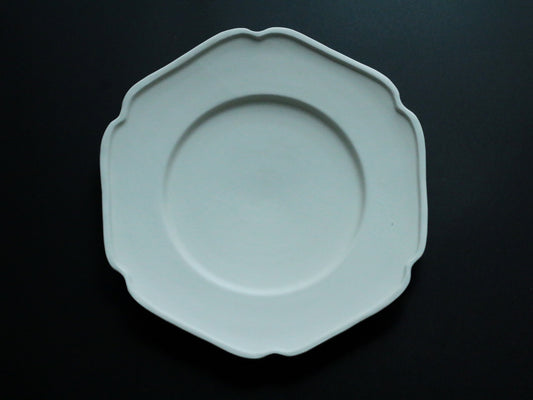 Round celadon plate with a softly scalloped edge and a raised inner ring, lit against black.
