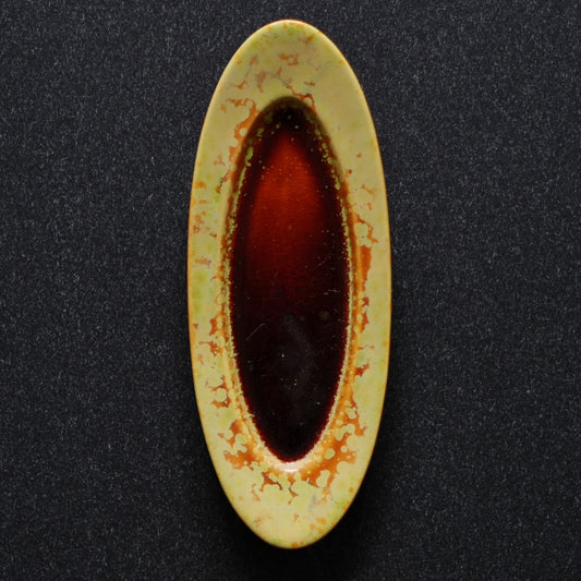 Narrow oval plate with a bright yellow rim and a deep pool of molten red-brown glaze at its centre.