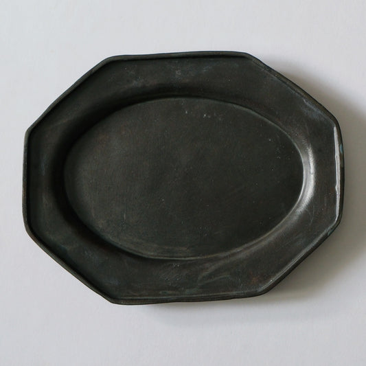 Octagonal plate in dark matte grey with a broad flat rim, lit softly against white.