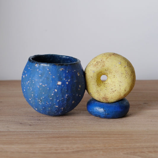 Speckled blue cup beside a yellow ring-shaped stand and a blue disc, on a wooden table.
