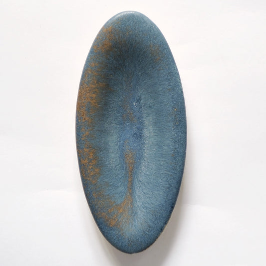 Long oval plate in dusty slate blue with rust-gold patches breaking across its matte surface.