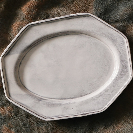 Octagonal plate in chalky off-white with a wide flat rim, on soft brown cloth.